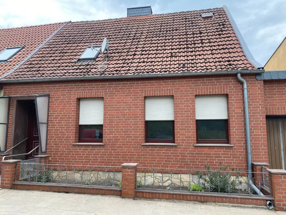 Ein rotes Backsteingebäude mit Garage und Nebengebäude im Hintergrund ist zum Kauf angeboten.